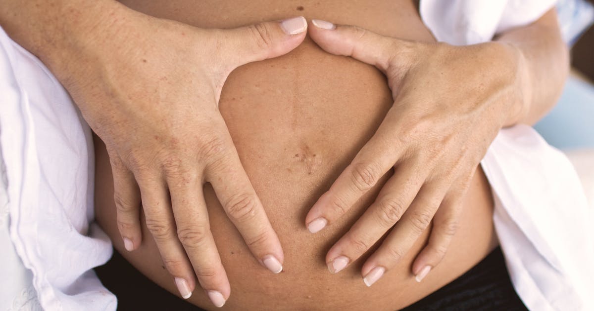 Gravid mage med händer som formar ett hjärta
