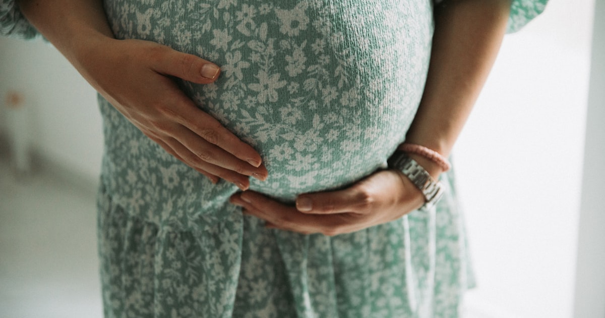 Gravid kvinna i grön klänning håller om magen