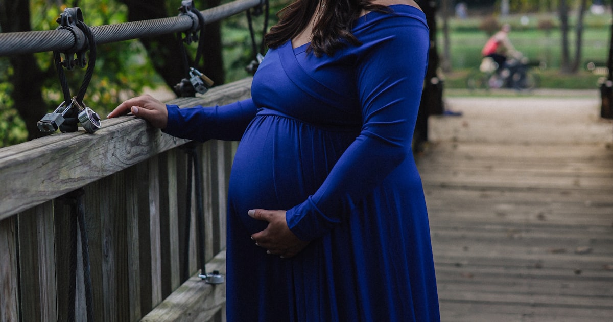 Gravid kvinna i klänning ler på träbro – stora storlekar
