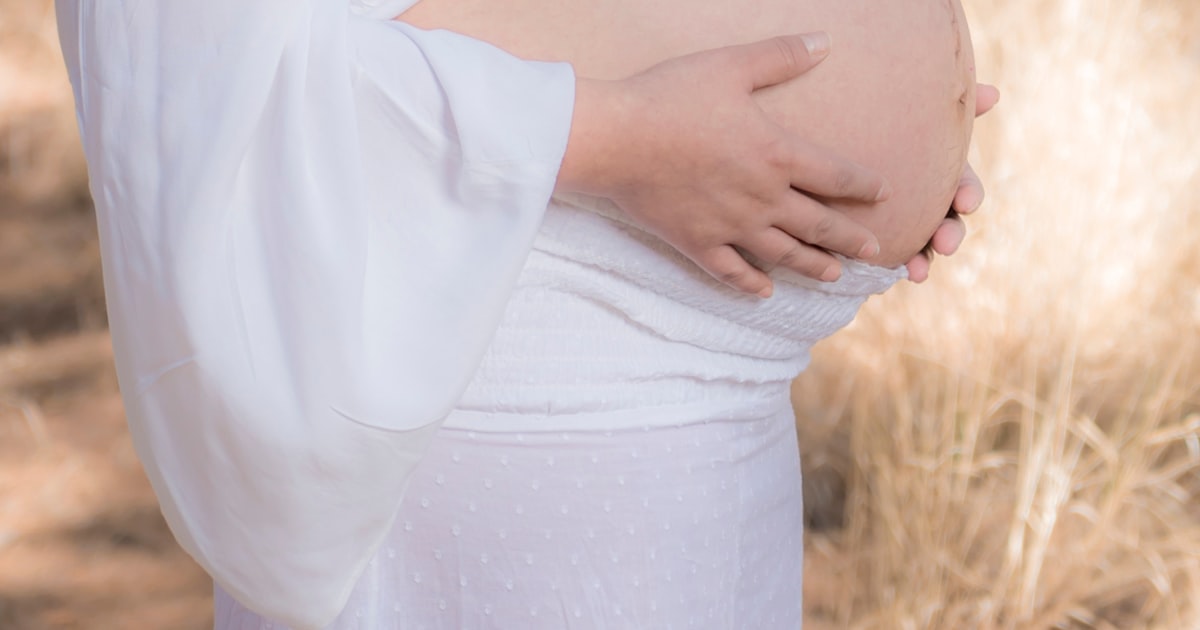 Gravid kvinna i vit omlottklänning – helkropp