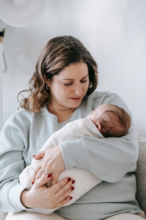 Lugn mamma i casual kläder kramar sin nyfödd på soffan