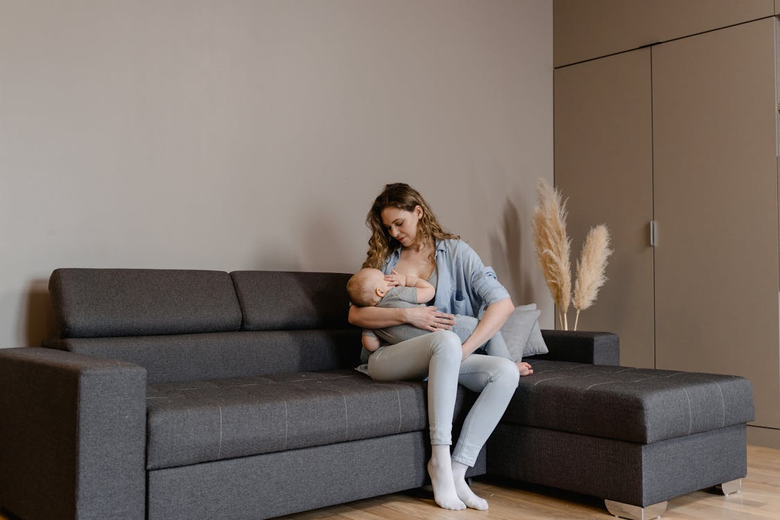 Kvinna ammar sitt barn i en amningstopp på soffa – illustration till artikel om cross-wrap vs drop-down amningstopp