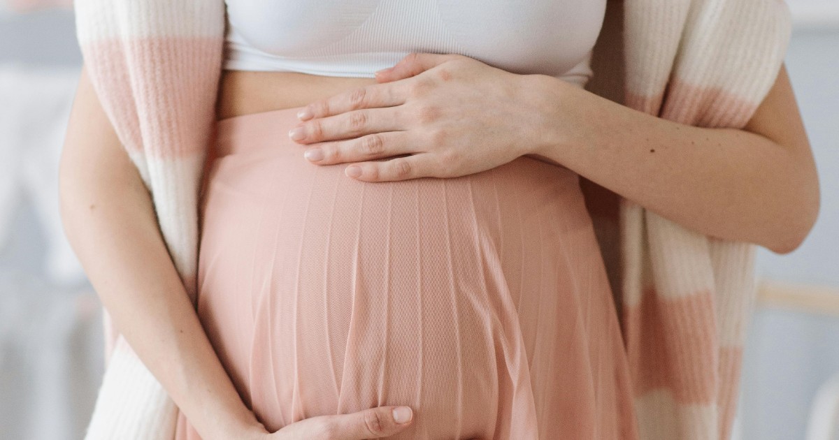 Gravid kvinna håller om magen iklädd vitt amningslinne med rosa kimono