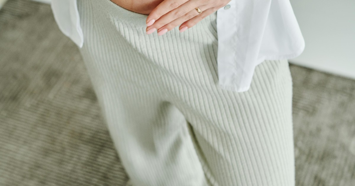Gravid kvinna håller om magen i vida vita gravidbyxor och gul top