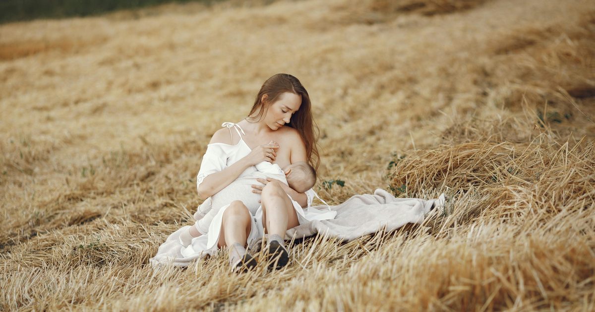 A serene portrait of a mother breastfeeding her baby in a peaceful rural field.